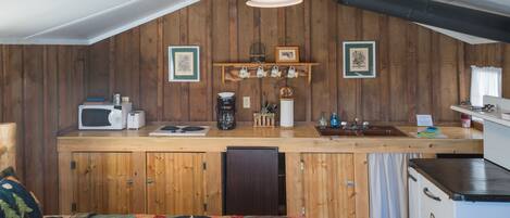 Et lille køkken med trævægge, en træbordplade, en mikrobølgeovn, en kaffemaskine og en vask.