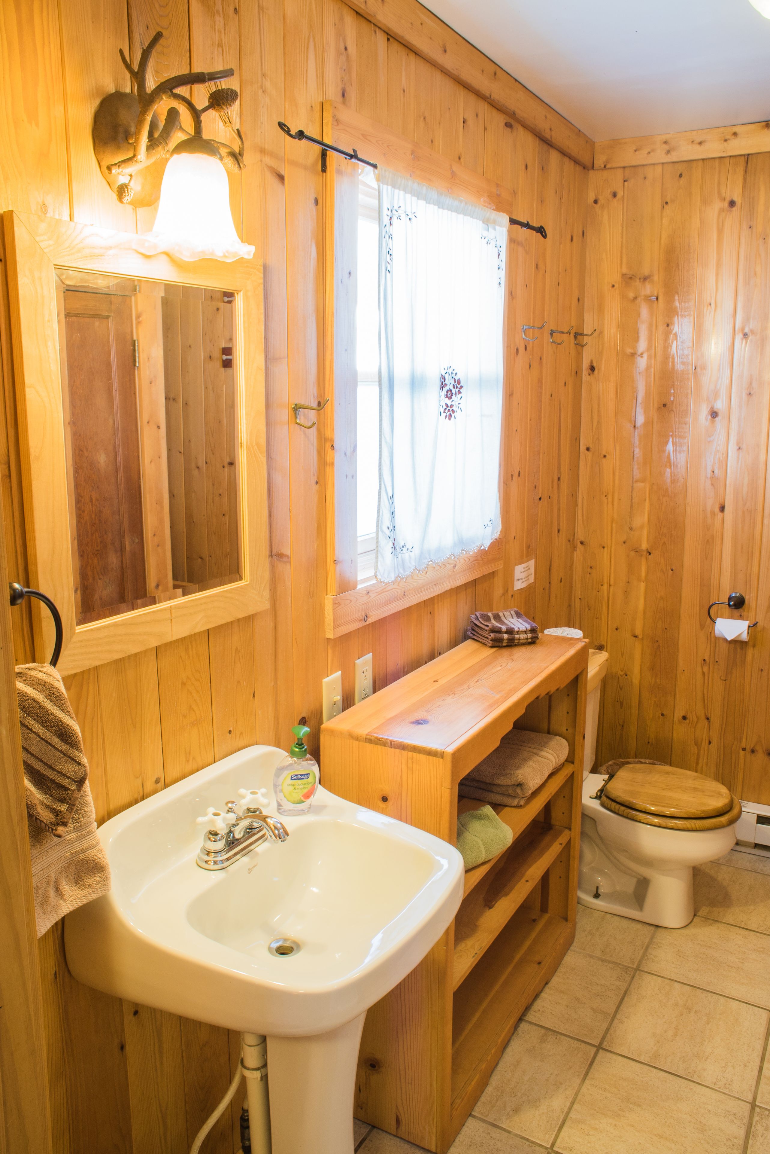 A wooden bathroom with a sink, mirror, and toilet.