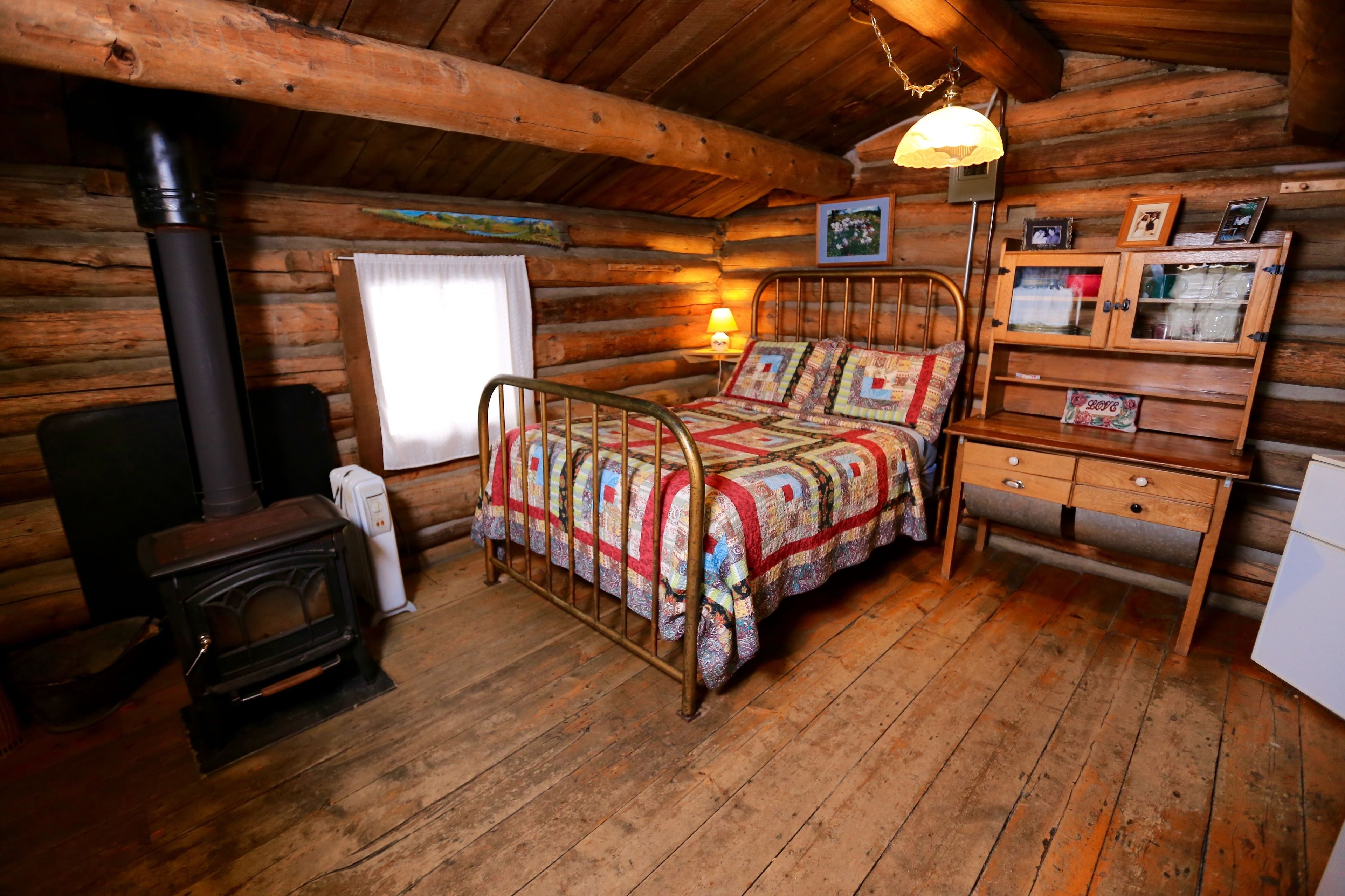 Acogedora habitación tipo cabaña de troncos con cama, cómoda de madera, lámpara y chimenea.