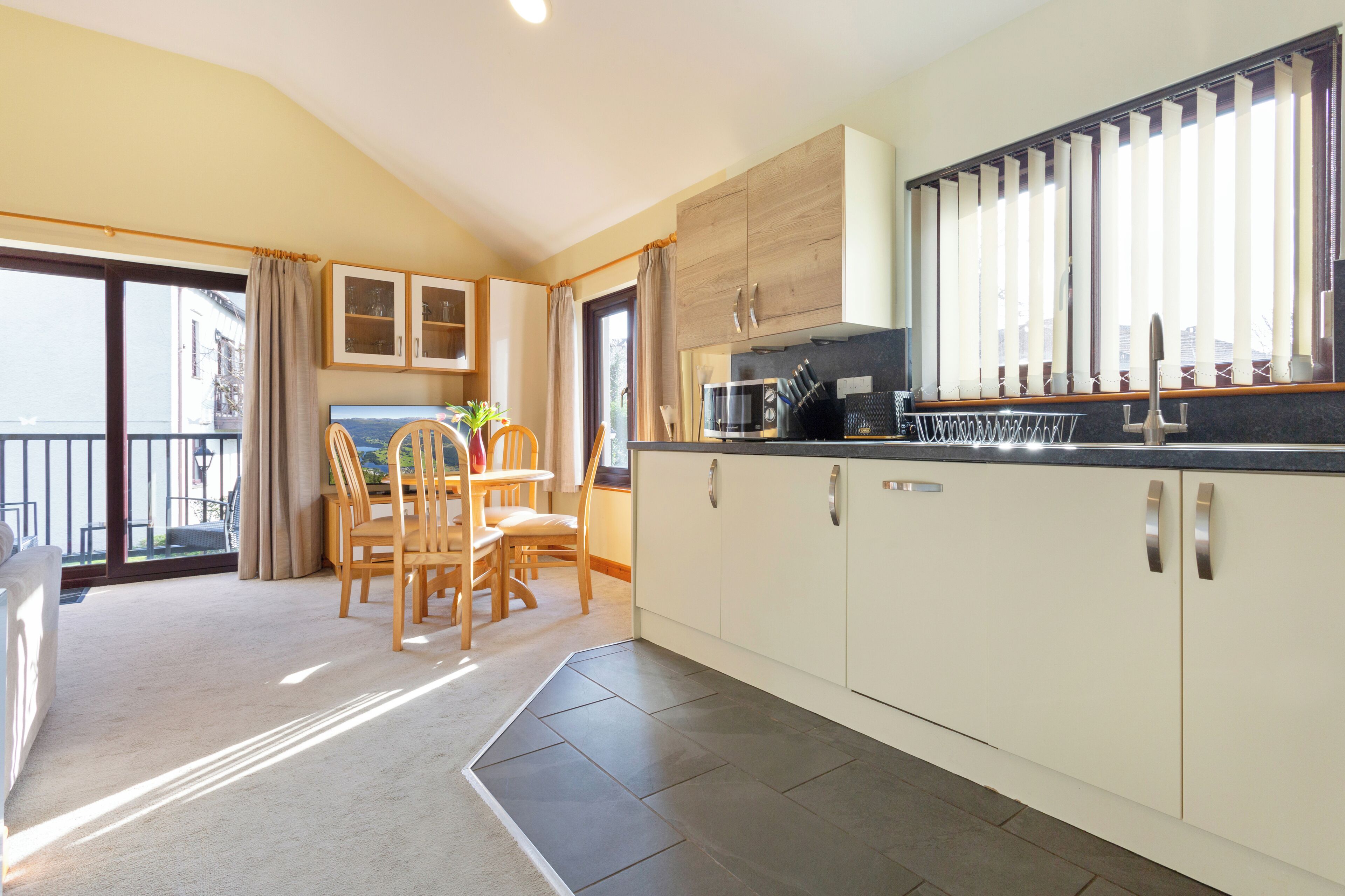 A modern kitchen with a dining area, large windows, and a view of the outdoors.