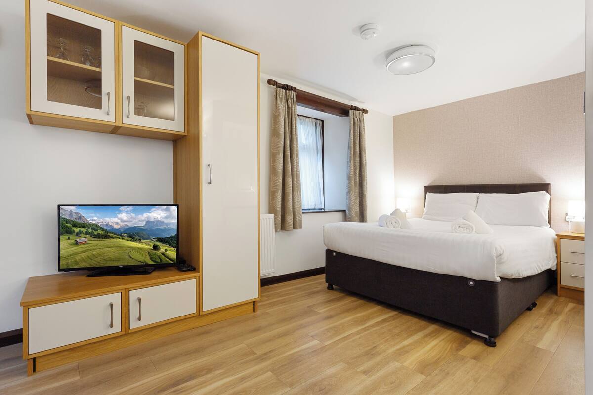 A hotel room with a bed, a television on a wooden cabinet, a window with curtains, and a ceiling light.
