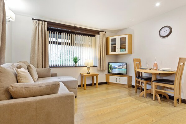 A living room with a sofa, TV, wooden dining table, chairs, and a cabinet.