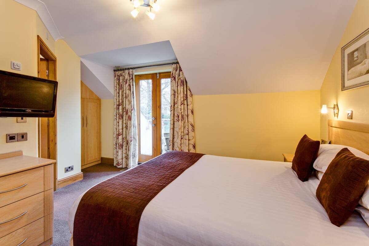 A hotel room with a bed, a television, a wardrobe, and a window with curtains.