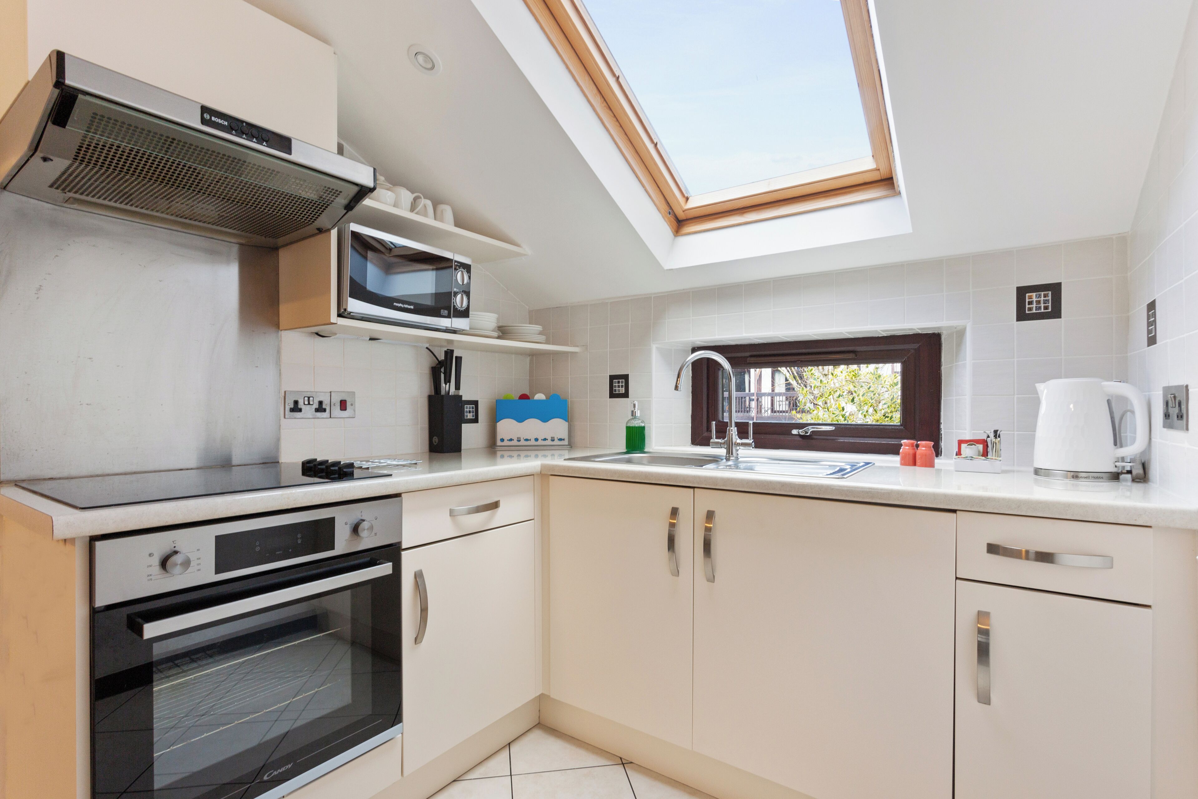 A modern kitchen with a skylight, built-in microwave, oven, and a sink with a window above.