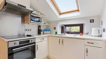 A modern kitchen with a skylight, built-in microwave, oven, and a sink with a window above.