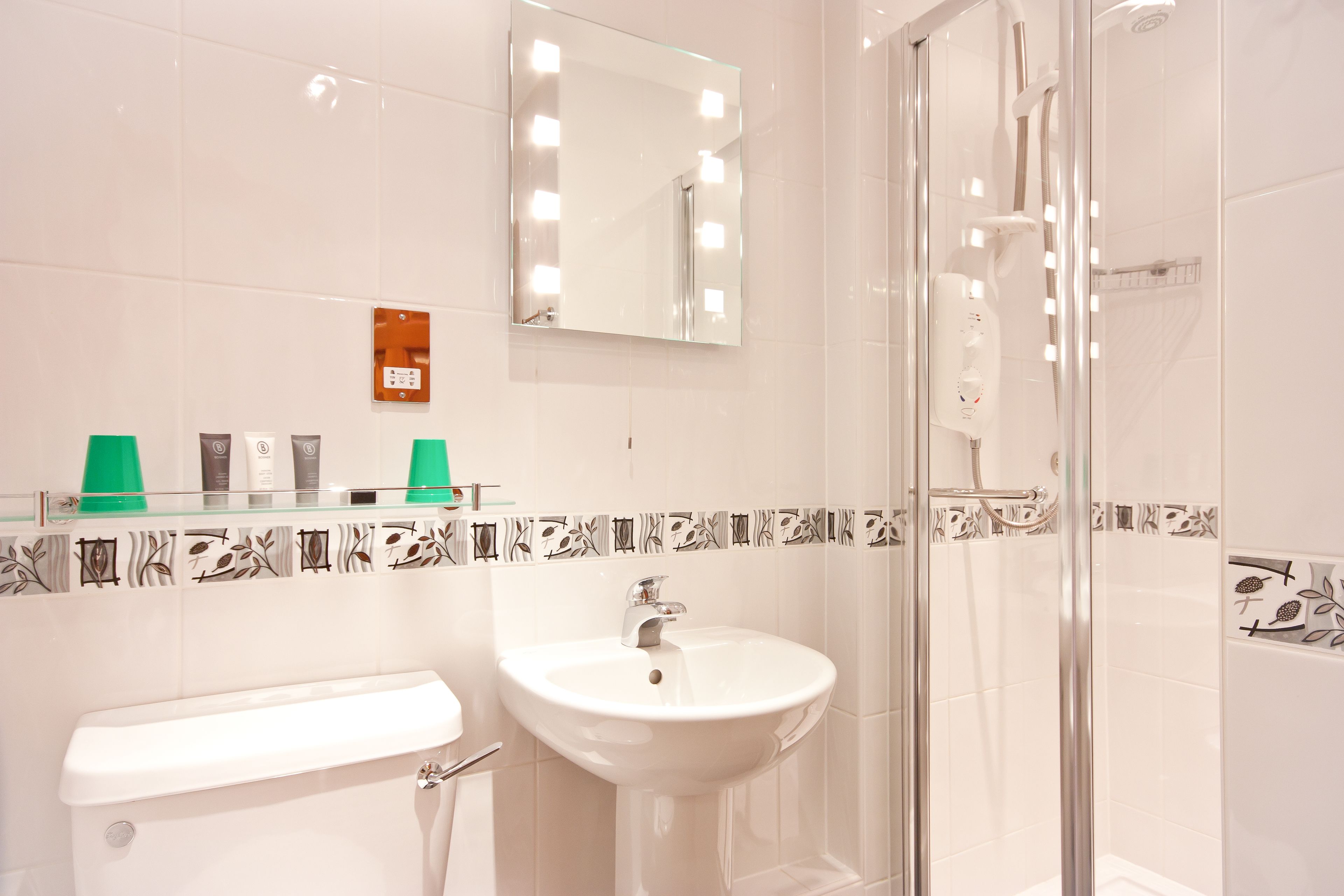 A bathroom with a white sink, a mirror with lights, a glass shower enclosure, and a toilet.