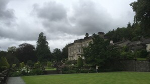 Um edifício grande e histórico com um jardim formal à frente.