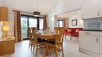 A dining area with a wooden table and chairs, a kitchen with white cabinets, and a red sofa in the background.