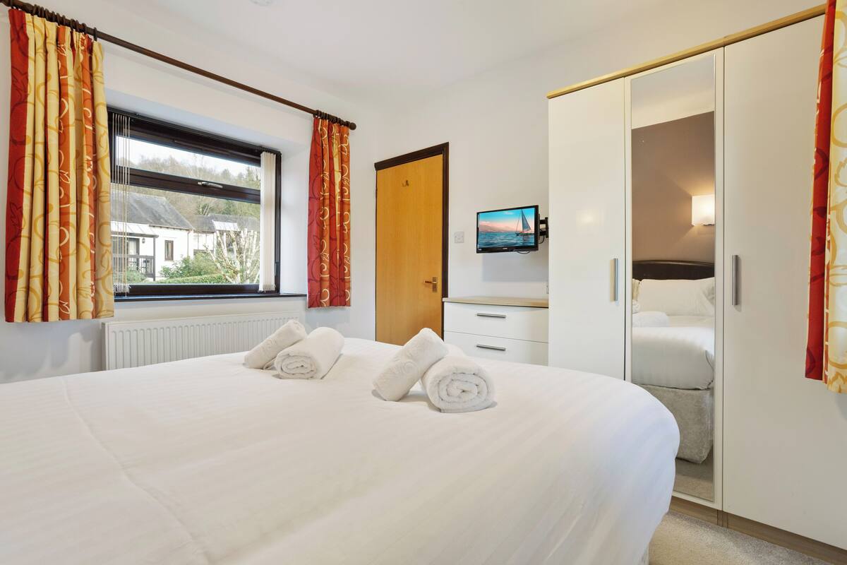 A hotel room with a large bed, a wardrobe, a television, and a window with curtains.