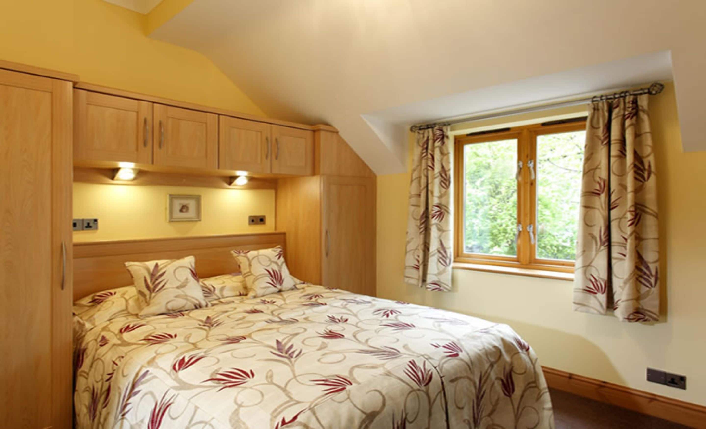 A bedroom with a bed, wooden wardrobe, a window with curtains, and a picture on the wall.