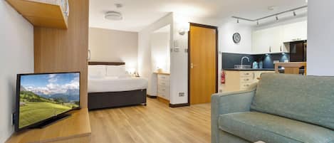 Una sala de estar moderna con una televisión de pantalla plana, un sofá, una cama y una cocina con un lavamanos y armarios.
