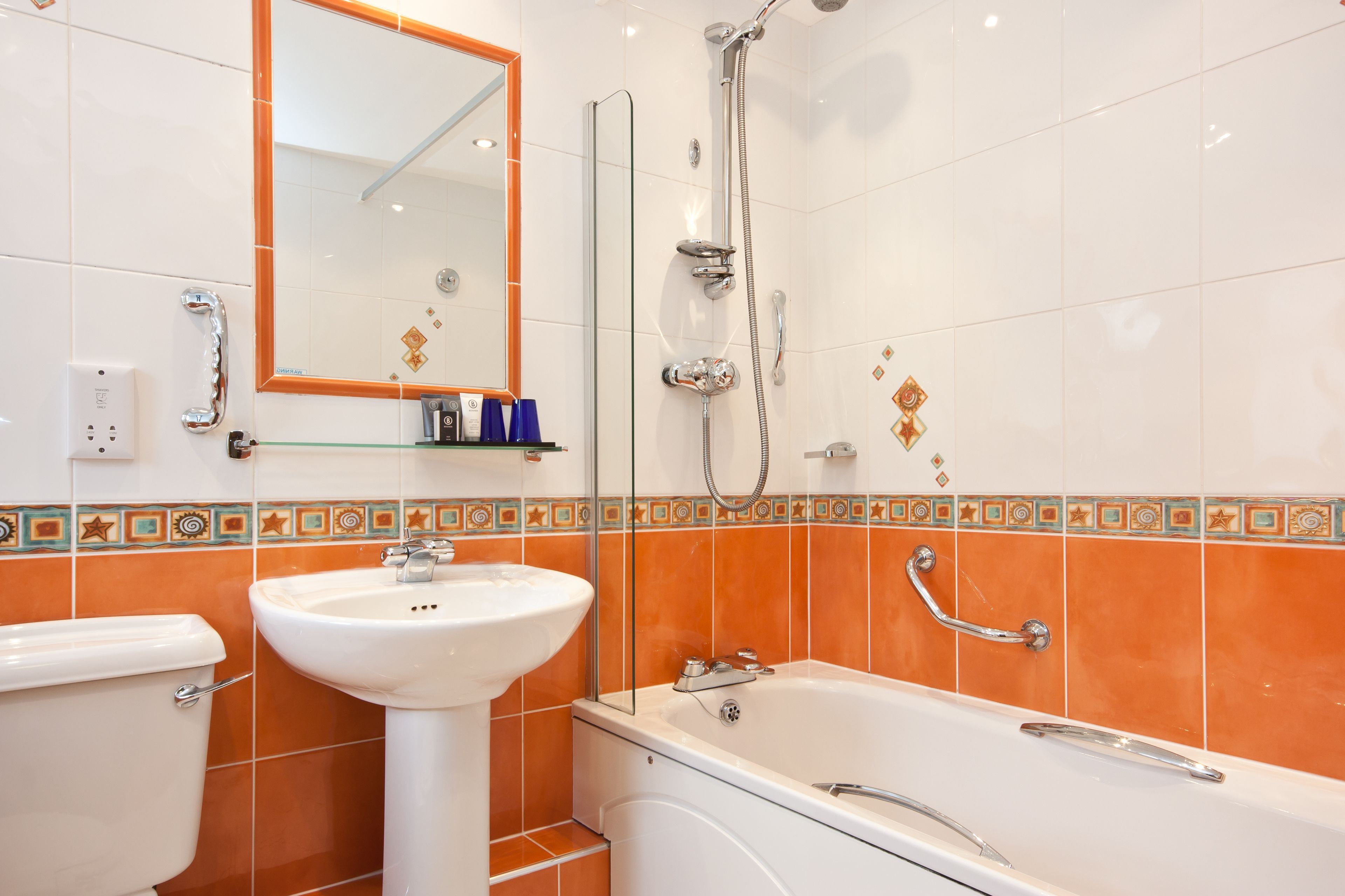 Un baño con lavamanos, inodoro y bañera blancos. Hay un cabezal de ducha y un espejo sobre el lavamanos.