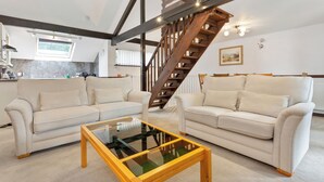 Uma sala de estar com dois sofás brancos, uma mesa de centro de vidro e uma escada de madeira.