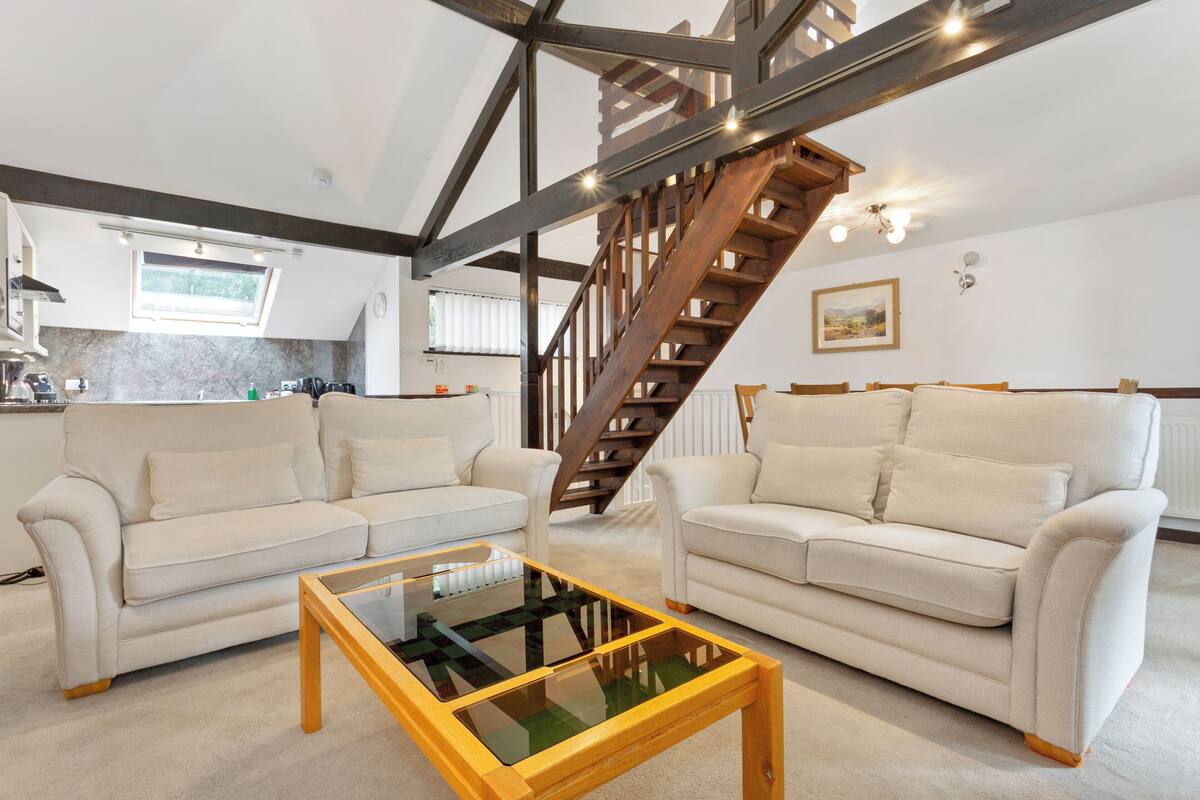 A living room with two white sofas, a glass coffee table, and a wooden staircase.