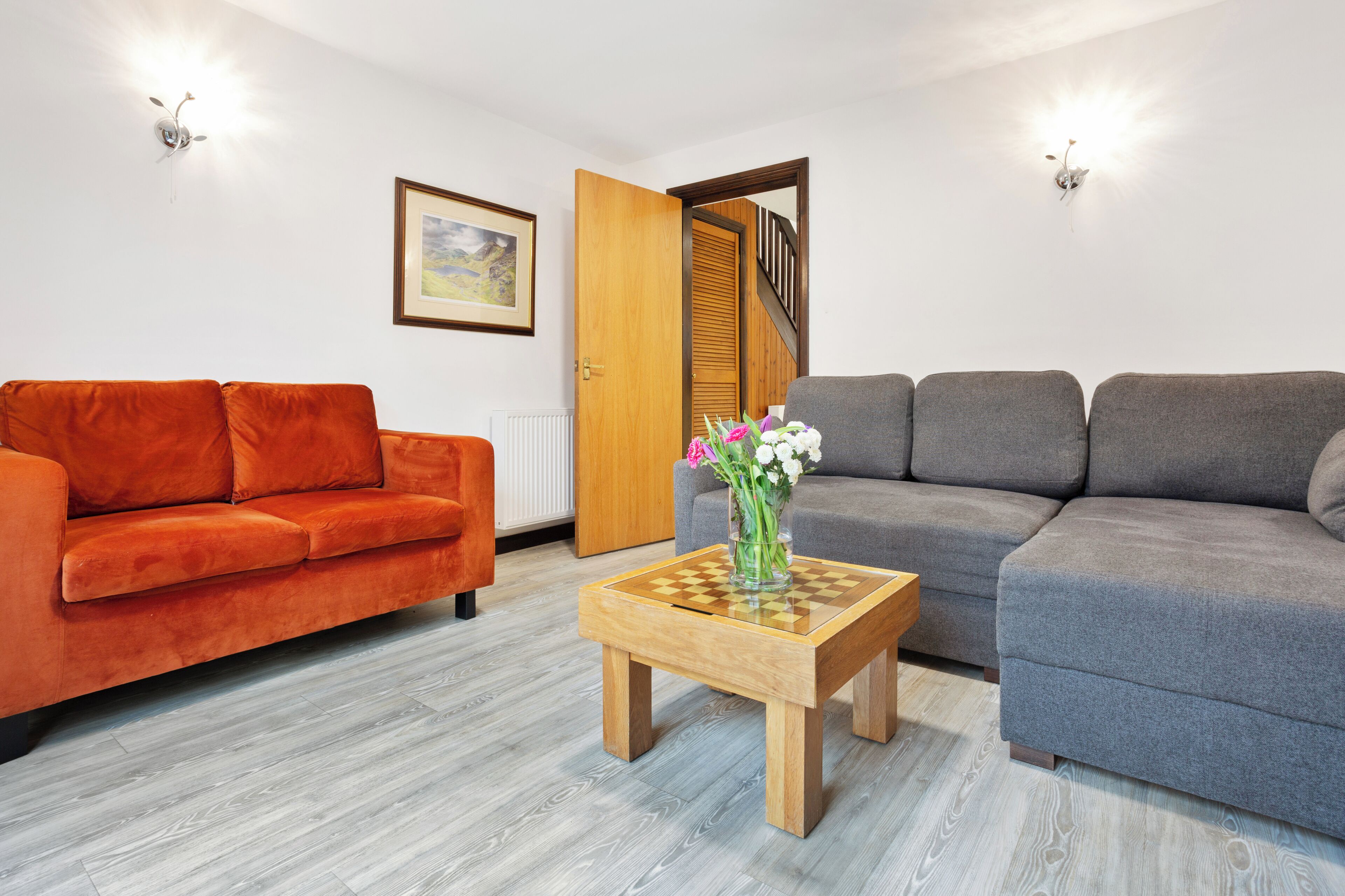 A living room with a wooden coffee table, orange and grey sofas, and a framed picture on the wall.