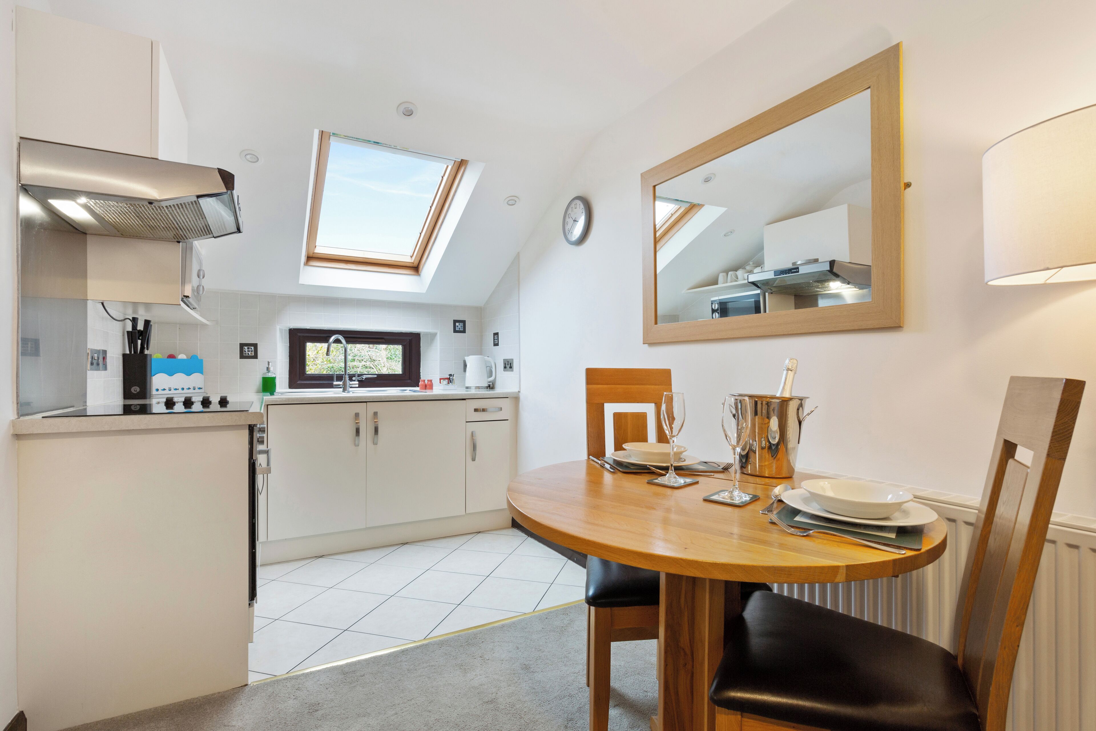 A compact kitchen with a skylight, a dining area with a table and chairs, and a large mirror on the wall.