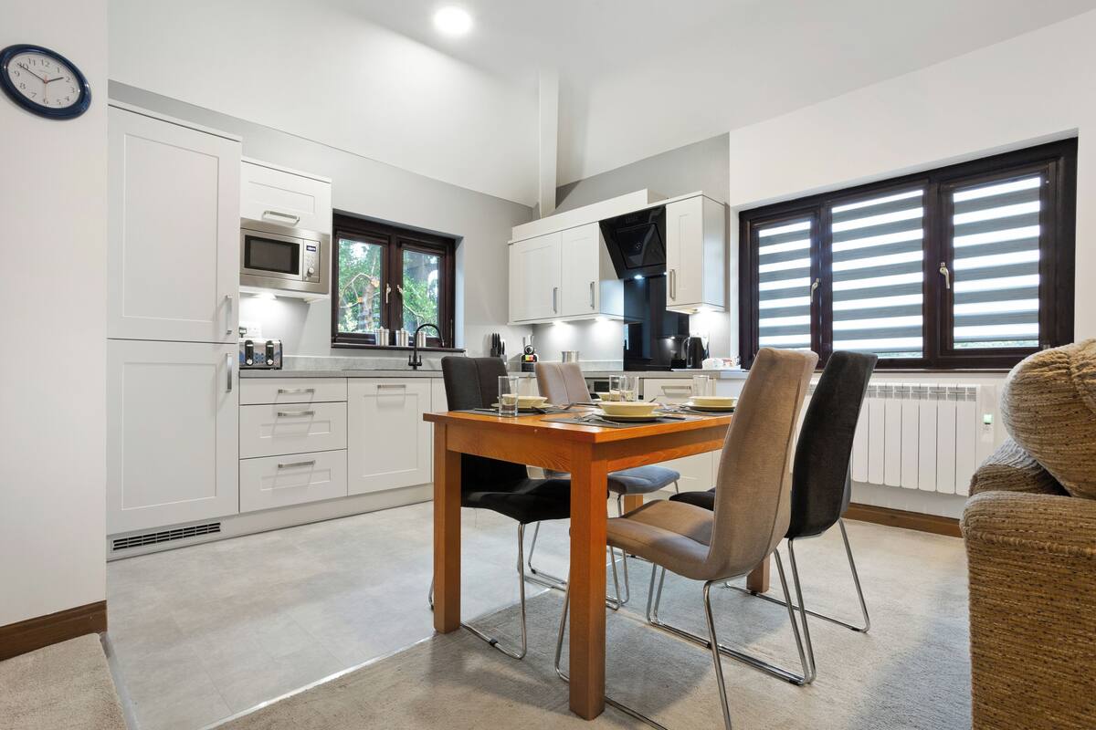 A modern kitchen with white cabinetry, a wooden dining table, and a window with blinds.