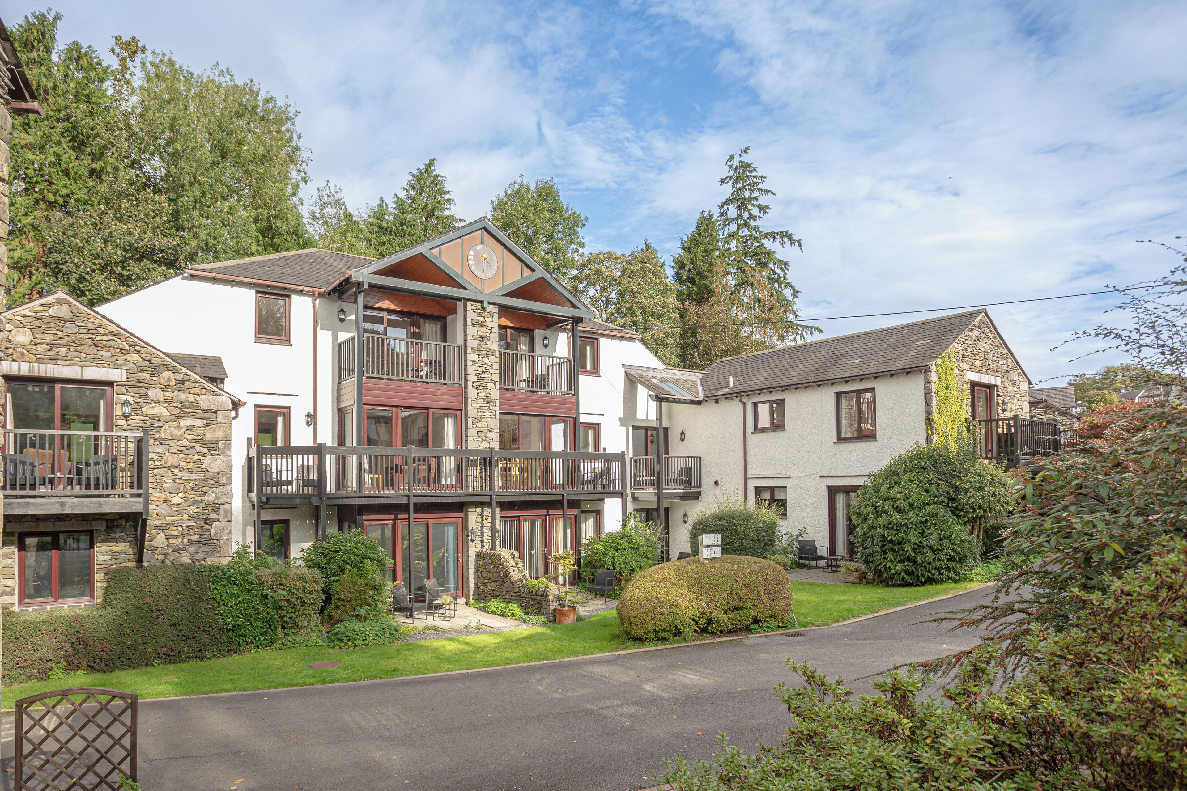 A multi-story building with a stone facade, balconies, and a well-maintained lawn.