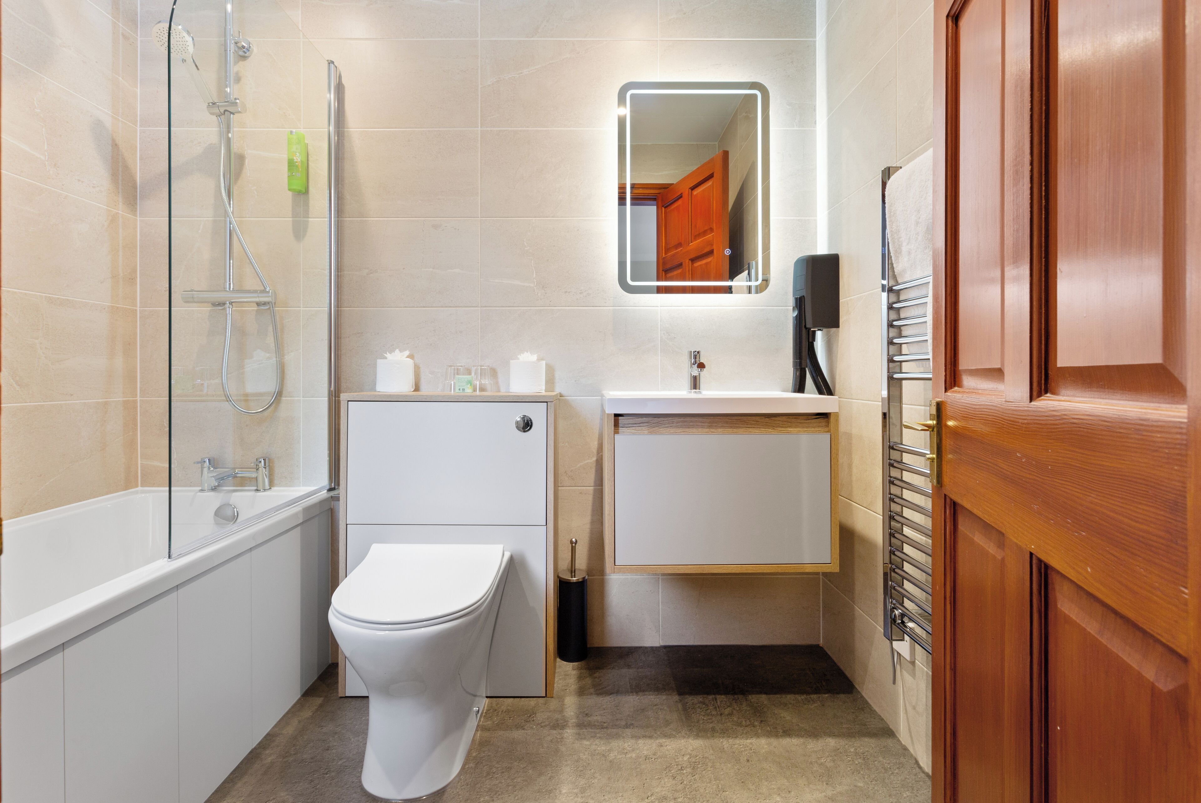 A modern bathroom with a white toilet, a glass-enclosed shower, a wooden vanity with a mirror, and a towel rack.