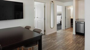 A modern hotel room with a dining area, a large mirror, and a kitchen.