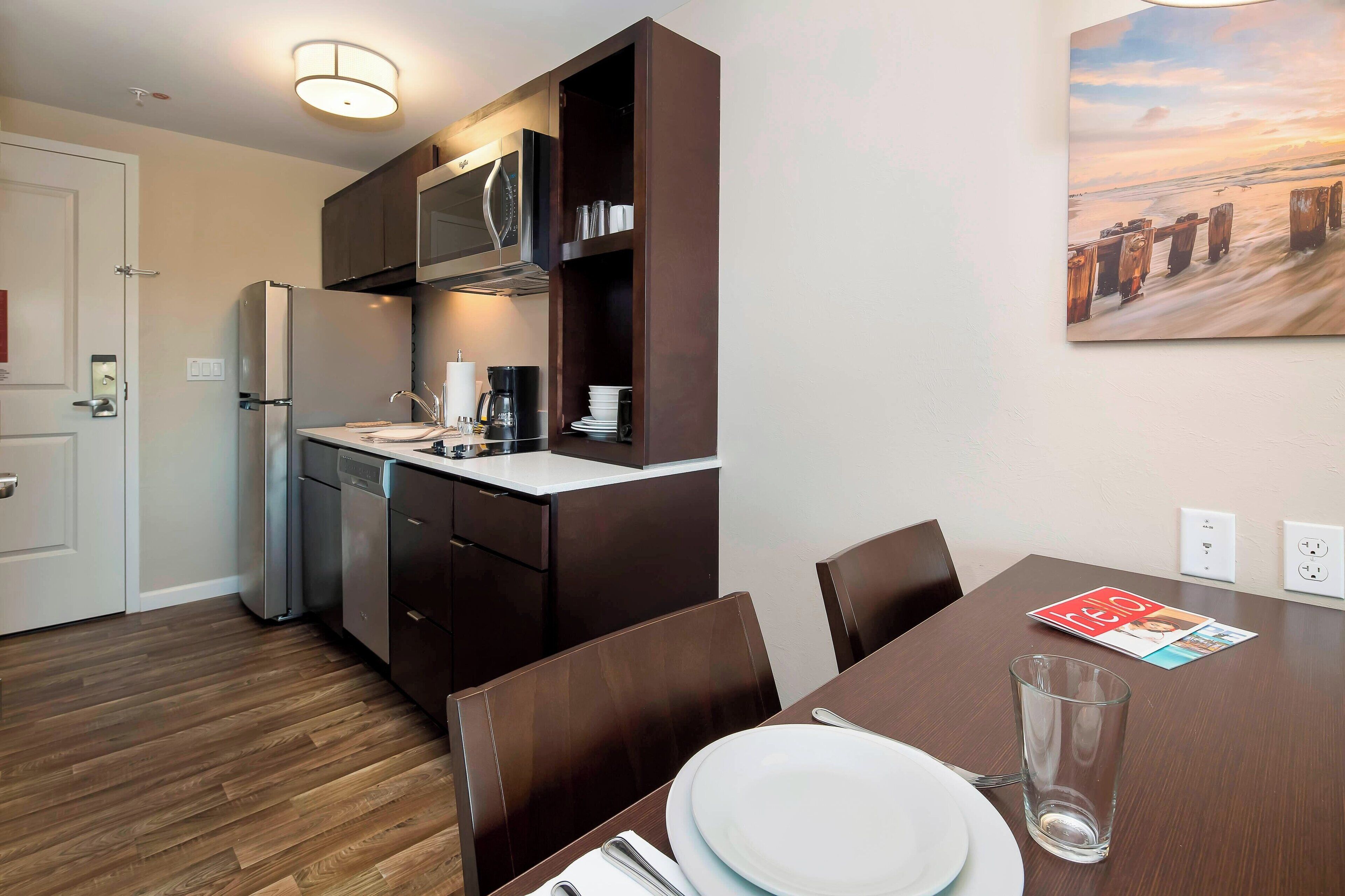 A modern kitchen with dark cabinetry, a stainless steel refrigerator, and a dining area with a table set for two.