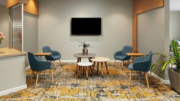 A conference room with a large flat-screen TV mounted on the wall, a round table with chairs, and a patterned carpet.