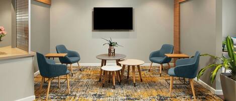 Een vergaderruimte met een grote flatscreen televisie aan de muur, een ronde tafel met stoelen en een kamerbreed tapijt met een patroon.