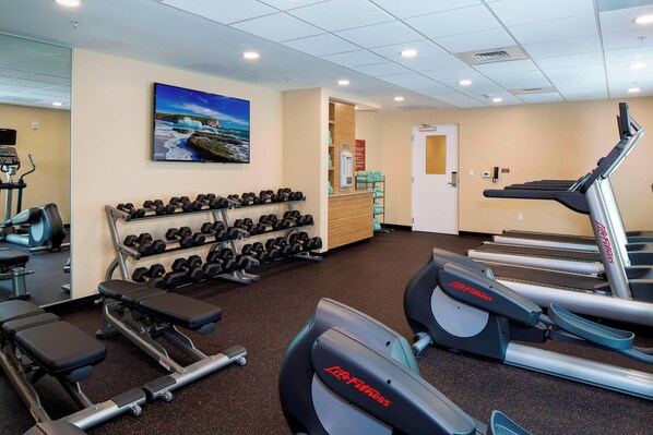 Un gimnasio con cintas de correr, pesas y un televisor montado en la pared.