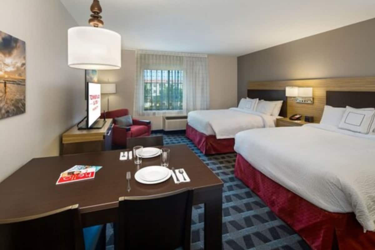 Een hotelkamer met twee bedden, een eettafel met stoelen, een bureau en een lamp.