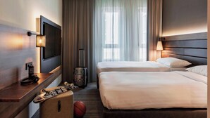 Habitación de hotel con dos camas, un televisor, un escritorio con lámpara, una maleta y un balón de baloncesto.