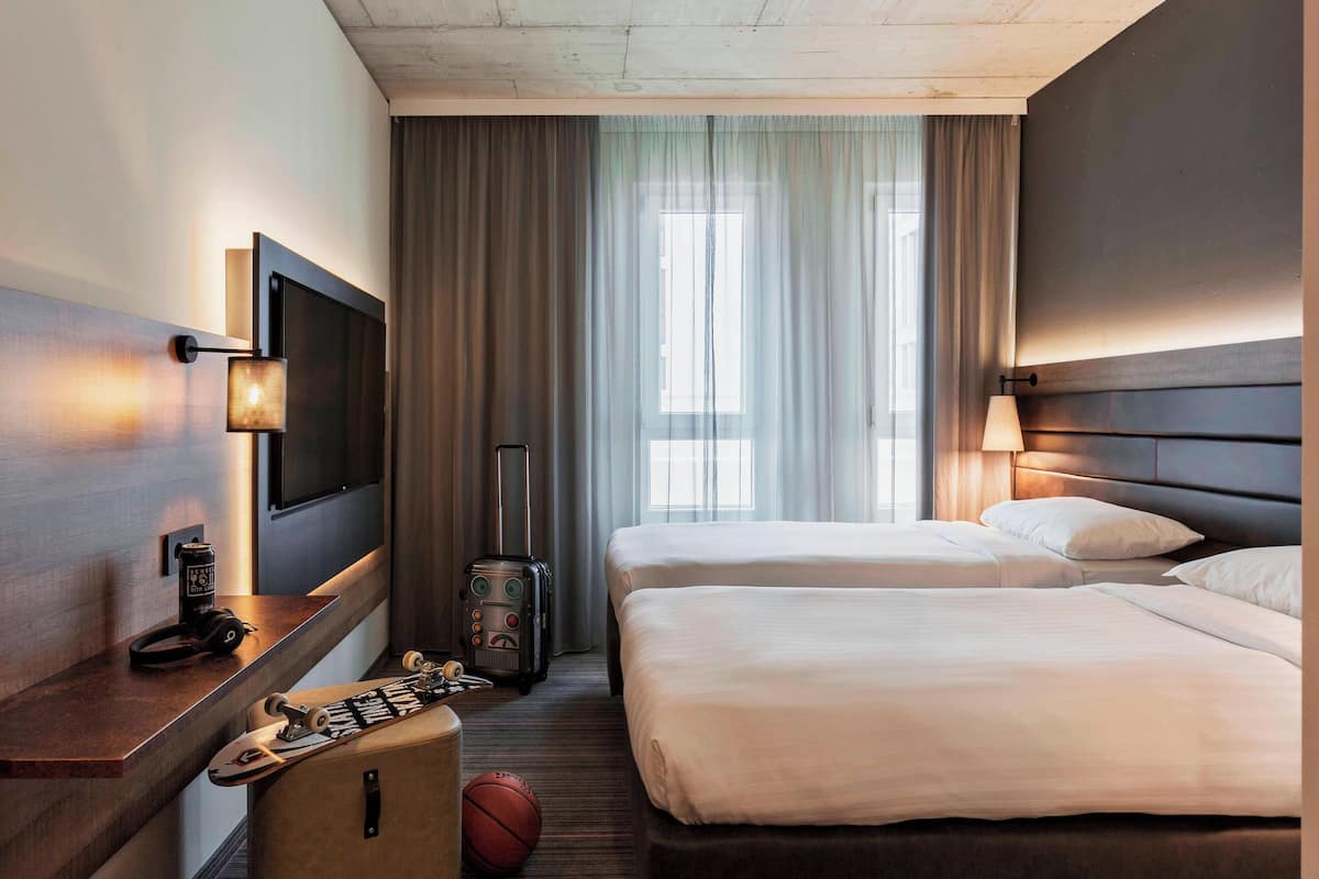Habitación de hotel con dos camas, un televisor, un escritorio con lámpara, una maleta y un balón de baloncesto.