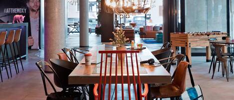 A modern dining area with a long table, orange chairs, and a foosball table.
