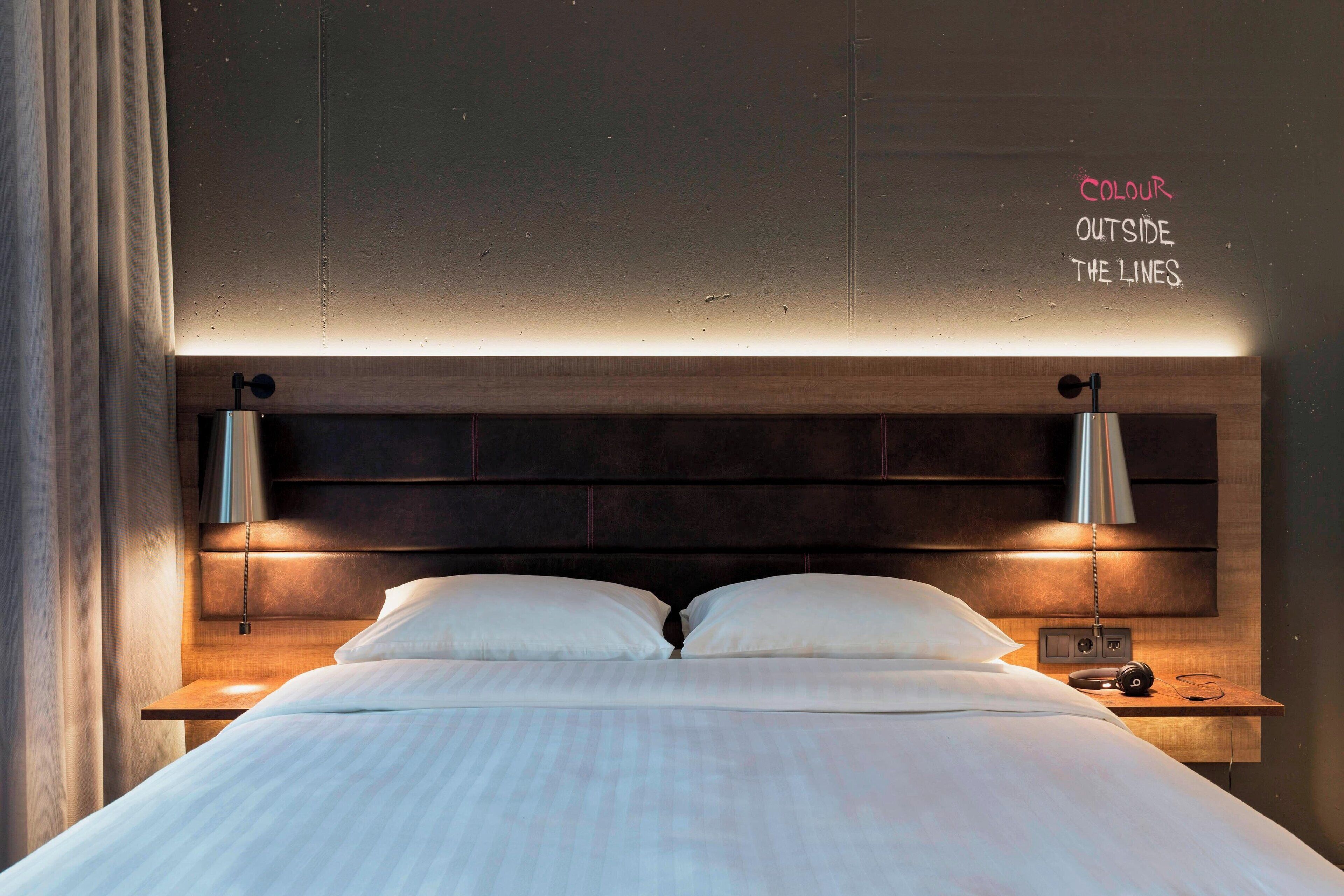 A neatly made bed with a wooden headboard, two bedside lamps, and a small table with a radio.