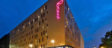 A modern hotel with a prominent neon sign, multiple floors, and a ground-level retail space.
