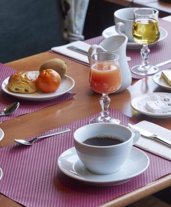 A dining table with a cup of coffee, a glass of orange juice, a croissant, and a small fruit. - Logis Hotel Du Lac (Huelgoat)