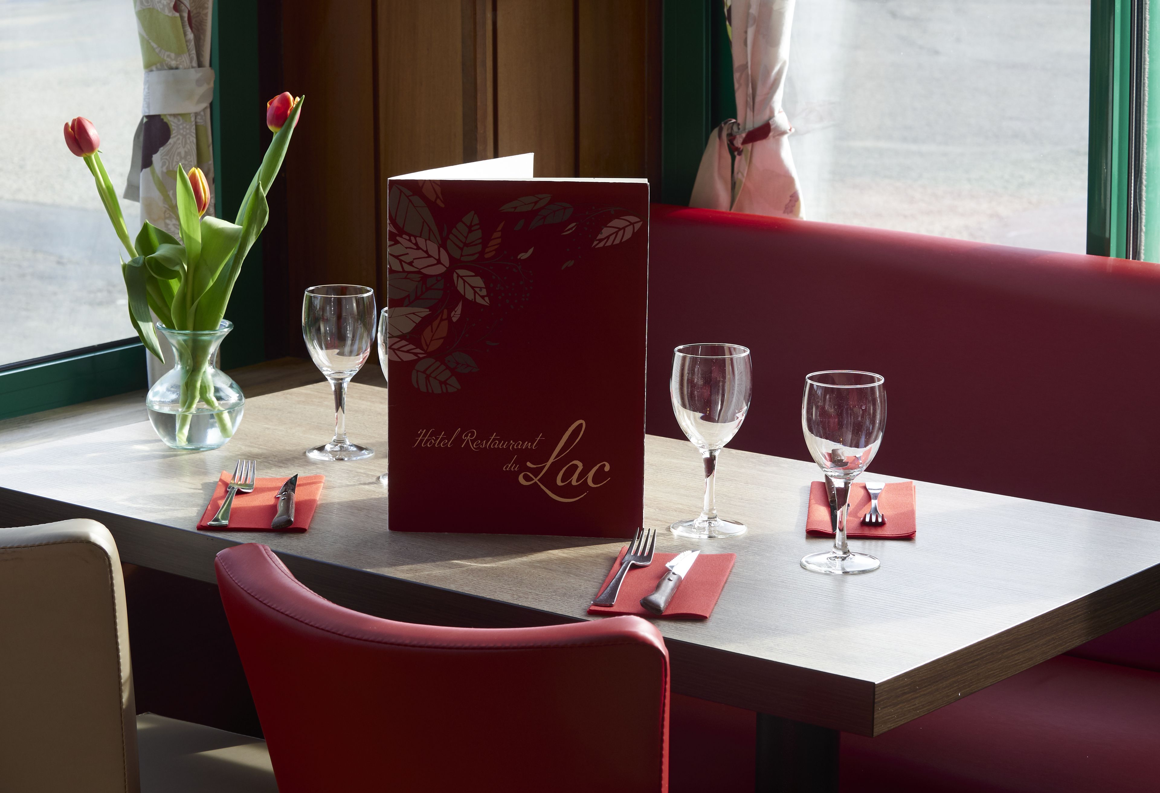 A dining table set with a menu, two wine glasses, a vase with tulips, and a red chair.