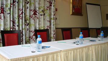 Une salle de conférence avec une longue table, des chaises rouges, des bouteilles d’eau et un tableau blanc.