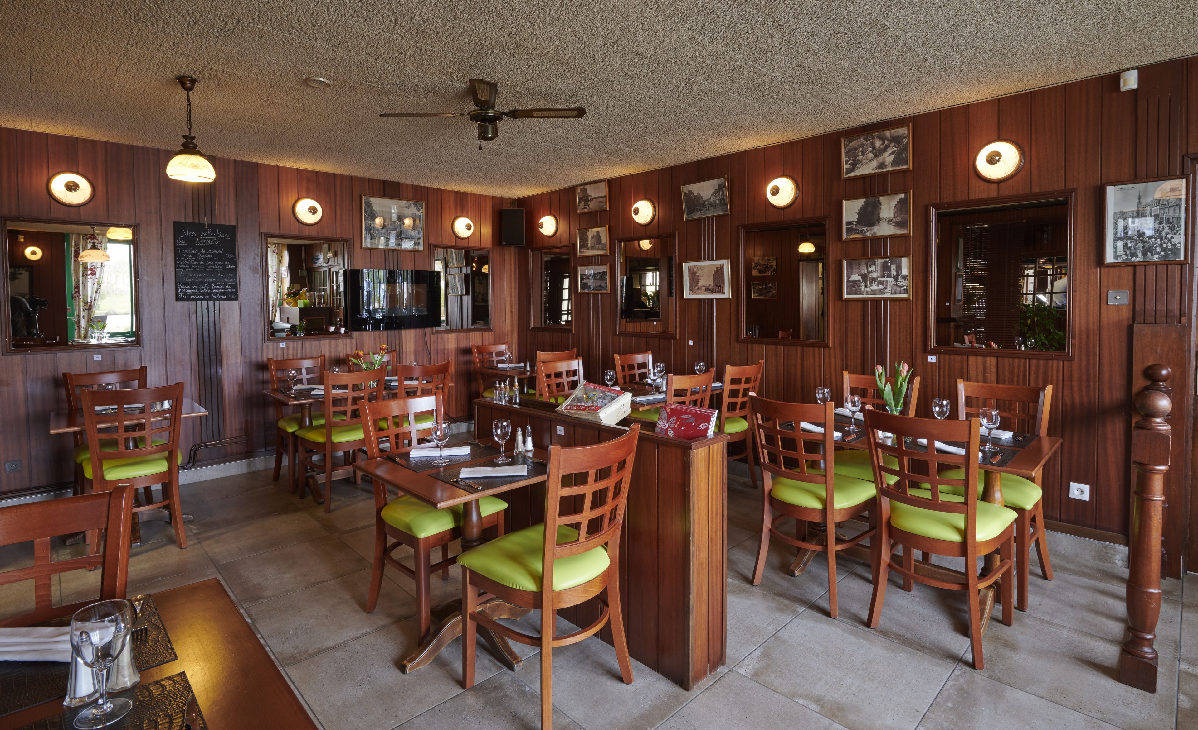 A restaurant with wooden paneling, green cushioned chairs, and a ceiling fan.