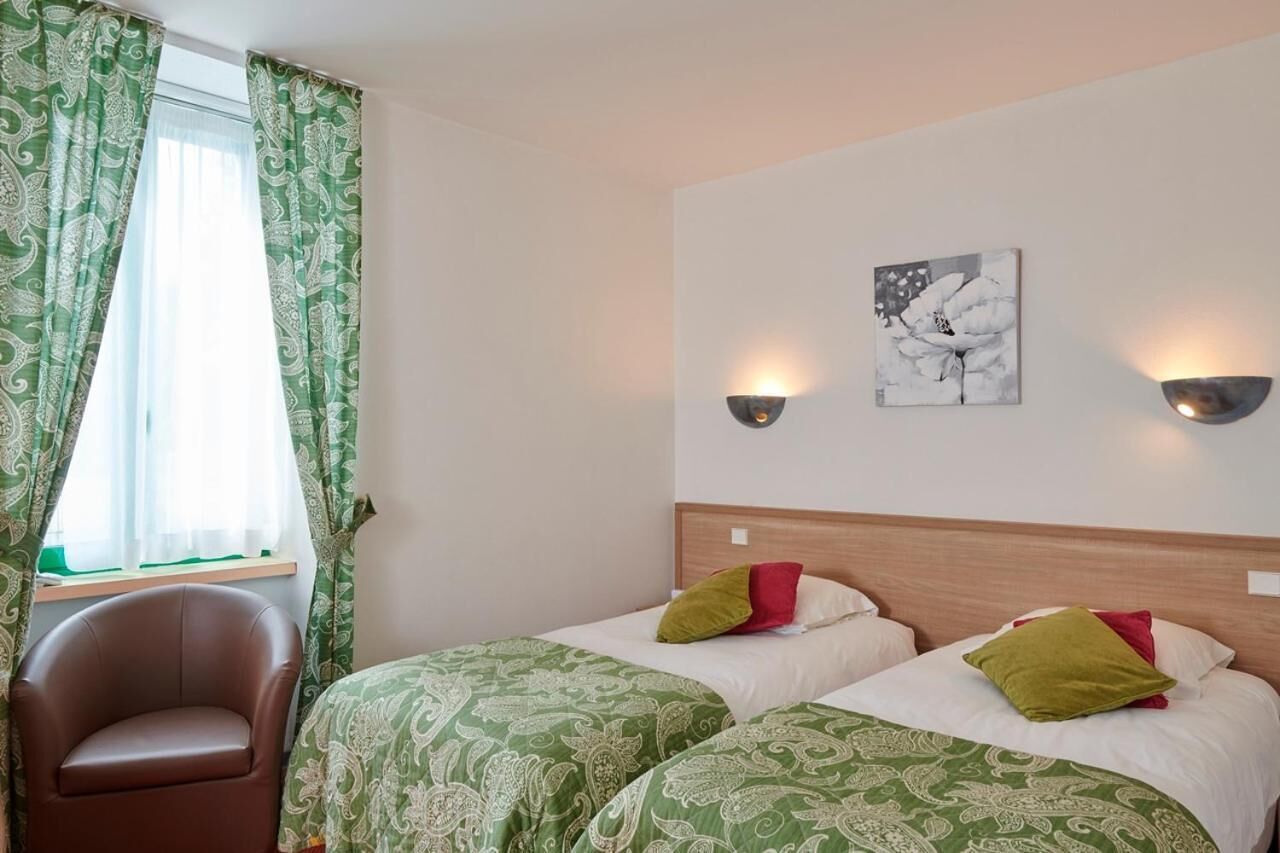 Habitación de hotel con dos camas, una silla, un ventanal con cortinas verdes y luces fijadas a la pared.