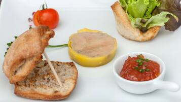 A plate with a slice of bread, a round meat slice, a cherry tomato, a lettuce leaf, and a small bowl of sauce.