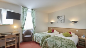 Una habitación de hotel con dos camas, un escritorio, una silla, un televisor y una ventana con cortinas.