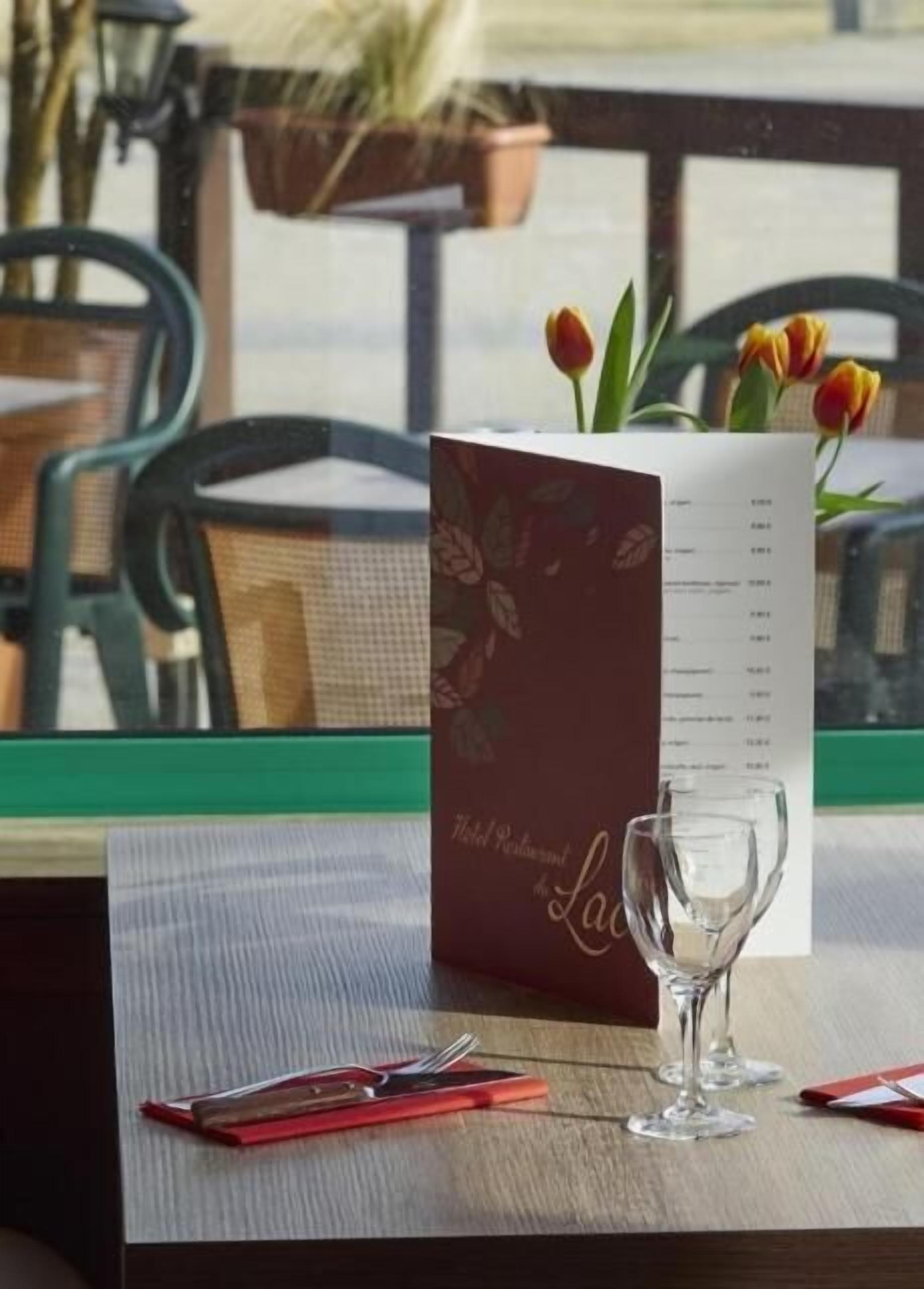 A table with a menu, a glass, and a red napkin holder.