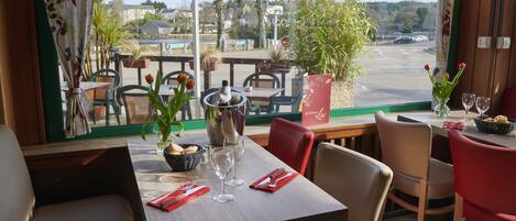 Un restaurant avec une table dressée pour deux personnes, un vase rempli de fleurs et une vue sur la rue et les bâtiments environnants.