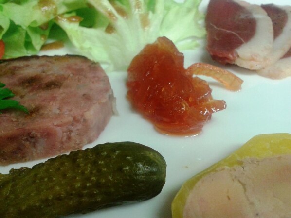 Un plato con diversos alimentos, incluyendo una porción de carne, un pepinillo y algunas verduras.