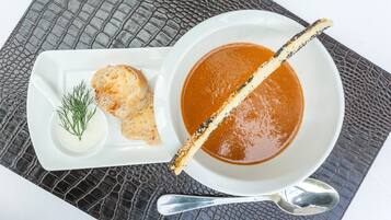 A white bowl of soup with a spoon and a piece of bread on a textured tablecloth.