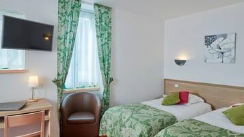 Ein Hotelzimmer mit Schreibtisch, Stuhl, zwei Betten, Fernseher und einem Vorhangfenster.