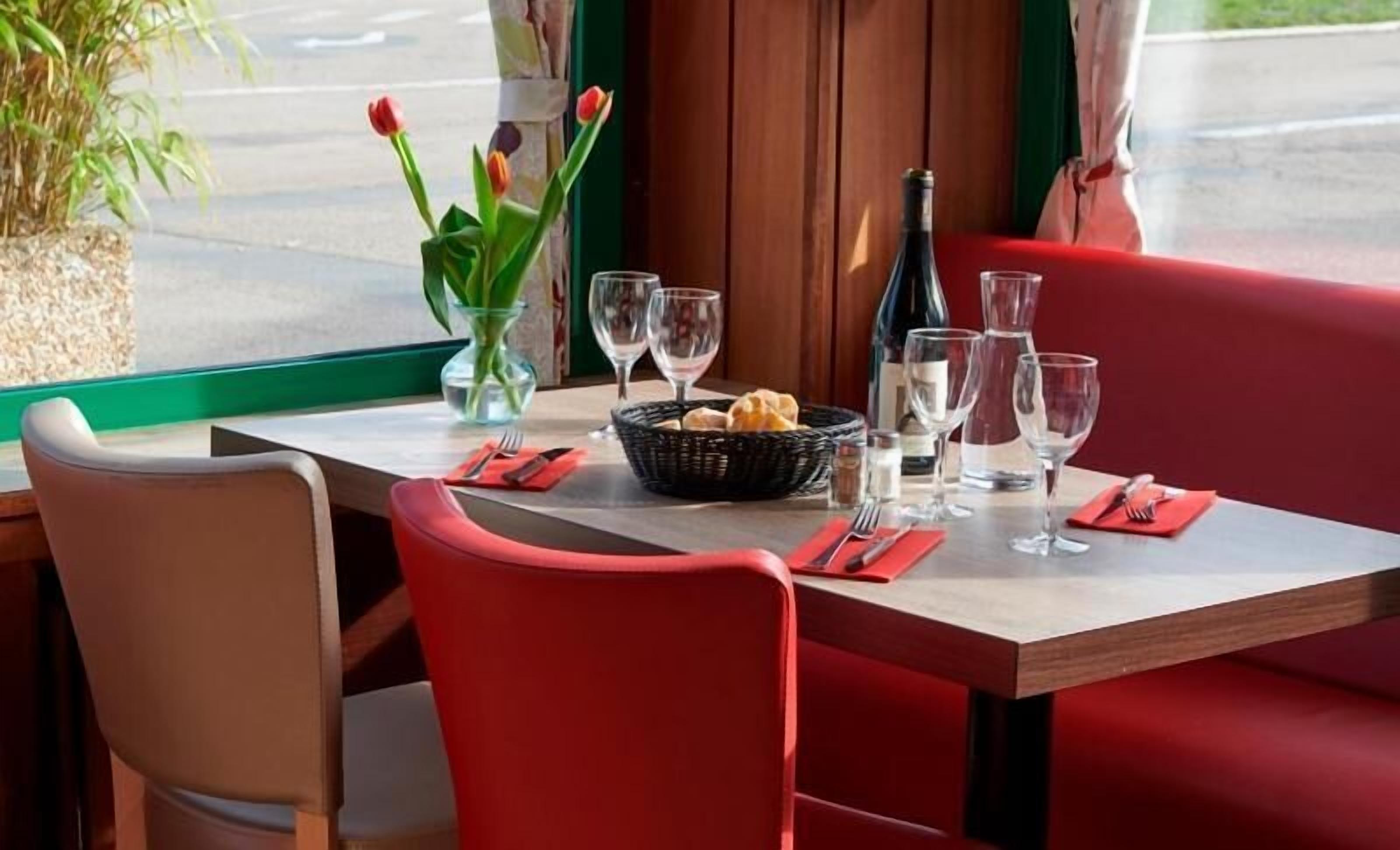 A dining table set with red upholstered chairs, a basket of bread, wine glasses, and a bottle of wine.