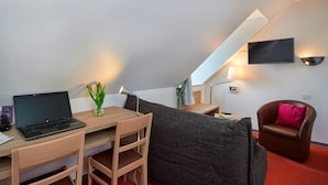 Habitación moderna y compacta con escritorio, laptop y un rincón de descanso acogedor con sofá y sillón.