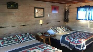 A room with two beds, each with a quilt, a lamp, a telephone, and a framed picture on the wall.