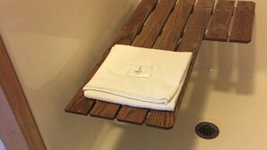 A bathroom with a wooden shelf holding a folded white towel and a small logo. - The Waters Inn (Gaylord)